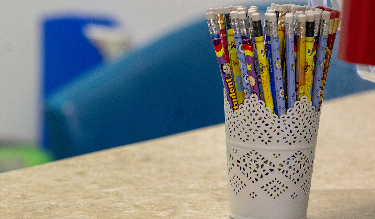 Colourful writing pencils with white erasers in a pretty cup on a desk.